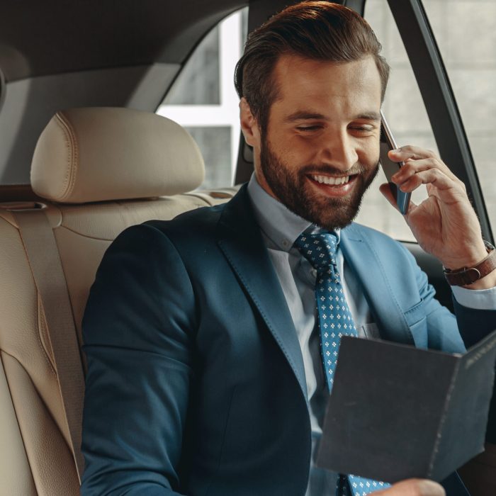 Close up front view portrait of laughing Caucasian founder in formal wear reserving table at the restaurant while traveling by a car